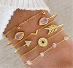 Gold bracelets with various designs on a wrist against a neutral background