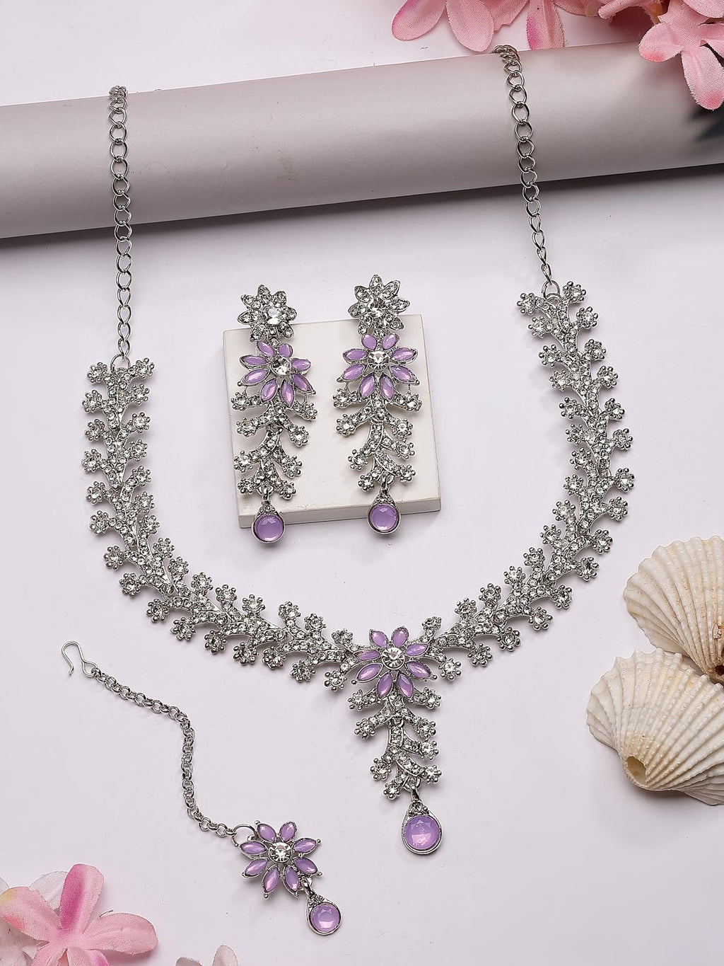 Jewelry set with necklace, earrings, and bracelet on a white surface with pink flowers and seashells.