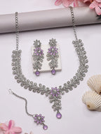 Jewelry set with necklace, earrings, and bracelet on a white surface with pink flowers and seashells.