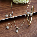 Gold jewelry set including necklace, ring, and earrings on a wooden surface.