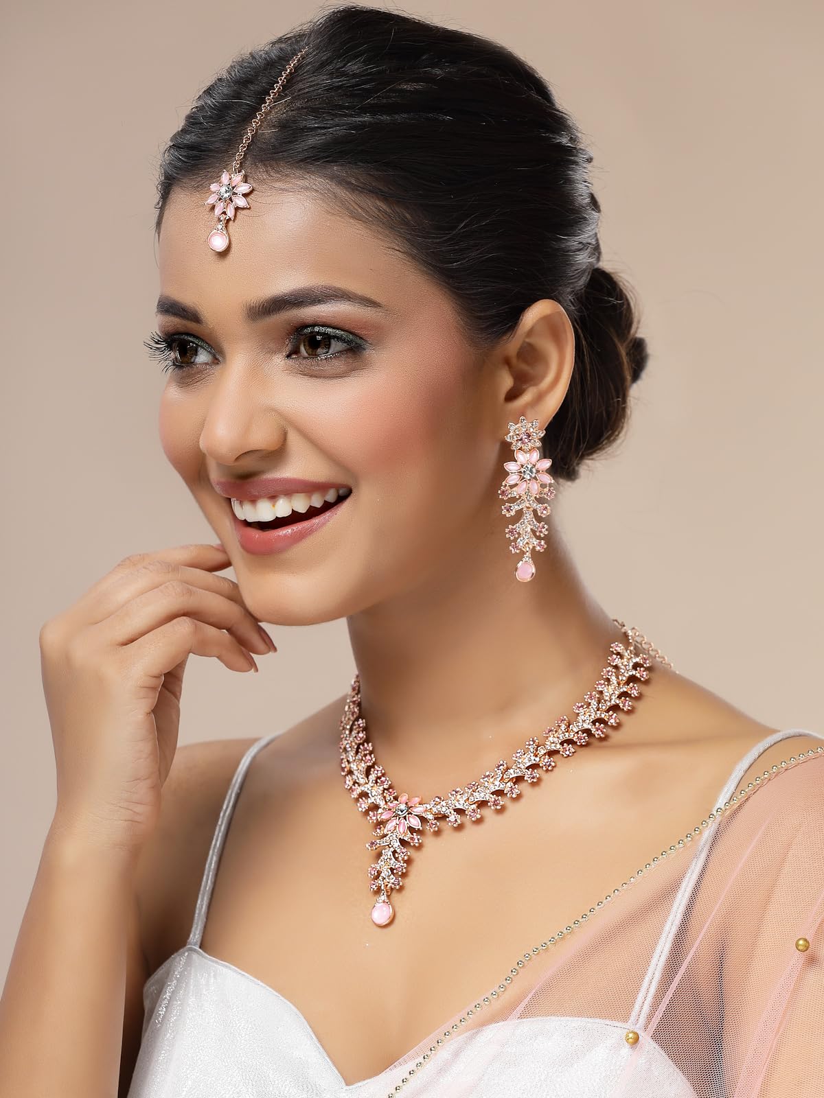 Woman wearing a rose gold necklace and earrings on a beige background