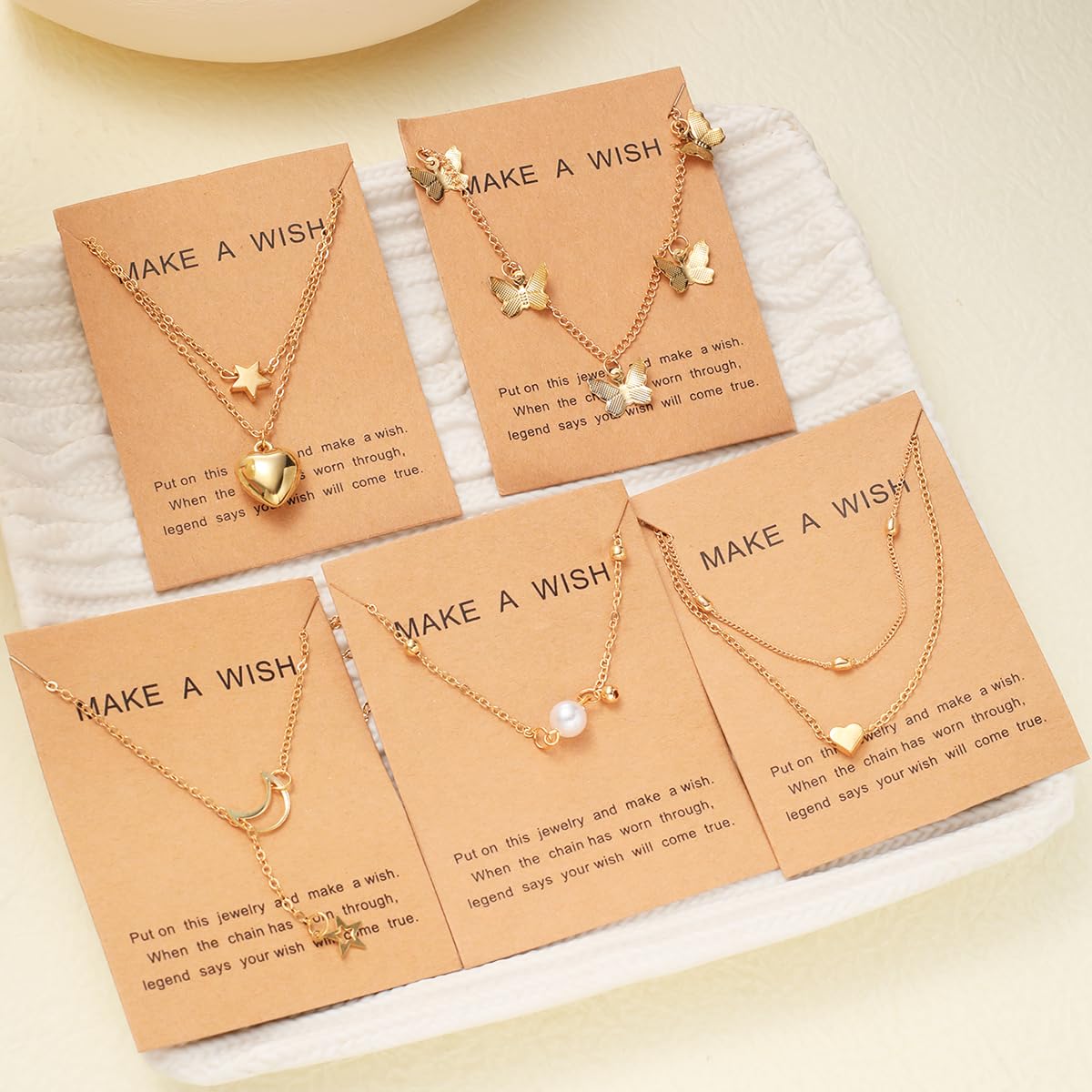 Gold necklaces on 'Make a Wish' cards with a soft beige background